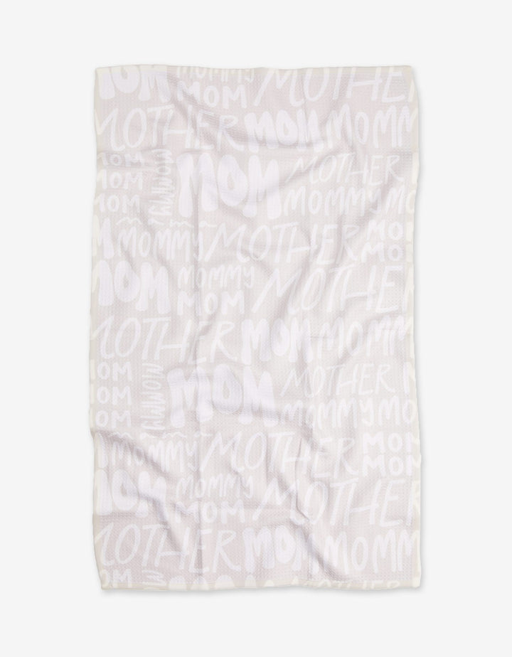 The GEOMETRY Mom blanket features white Geoweave fabric with repeated words MOM, MOTHER, and MOMMY in varied sizes and fonts in a light, semi-transparent print. The blanket is shown flat with some visible wrinkles.