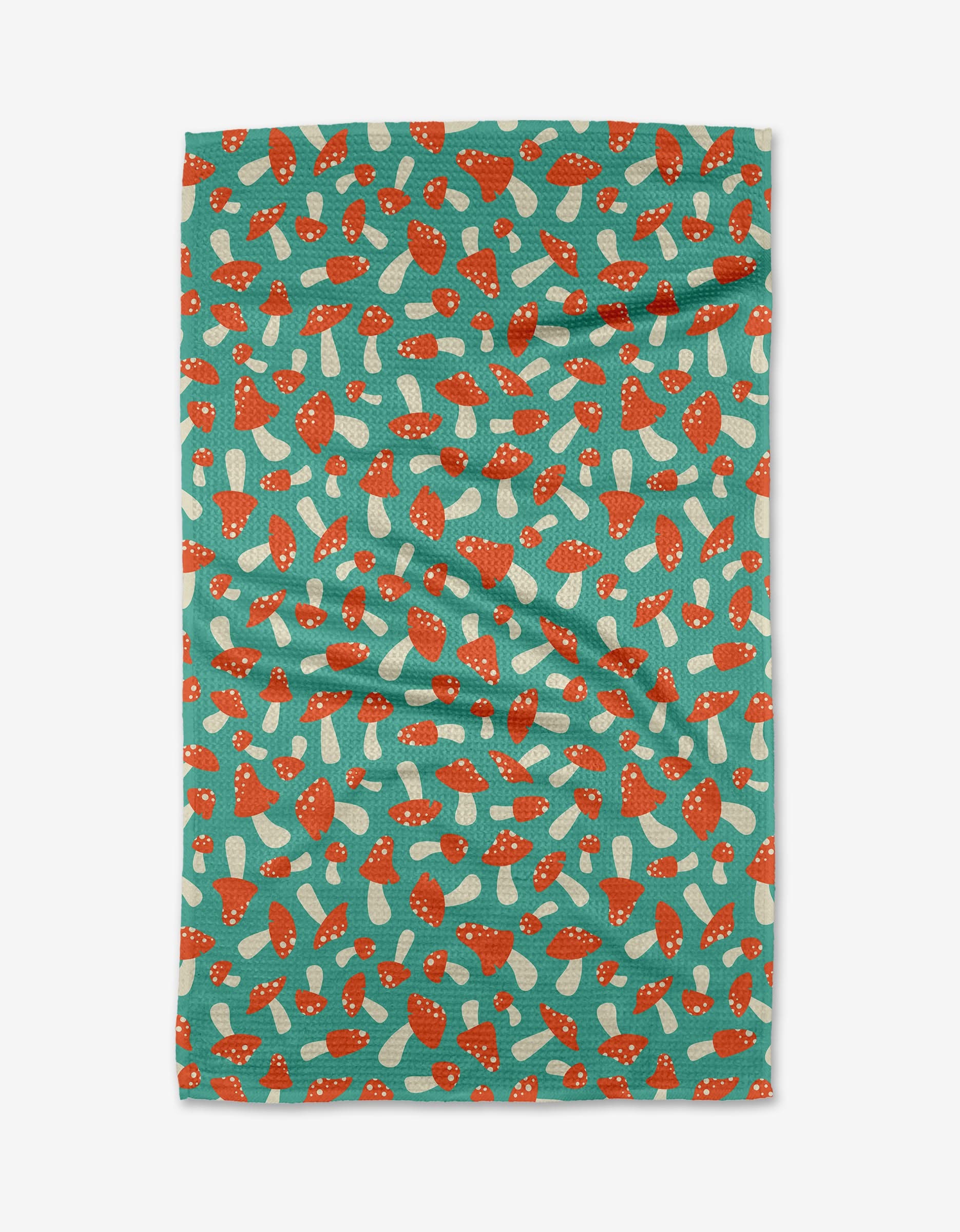 The “Mushrooms” tea towel by Megan Kampa is teal, crafted from recycled materials, and features a repeating pattern of red and white mushrooms on a lightly wrinkled surface.