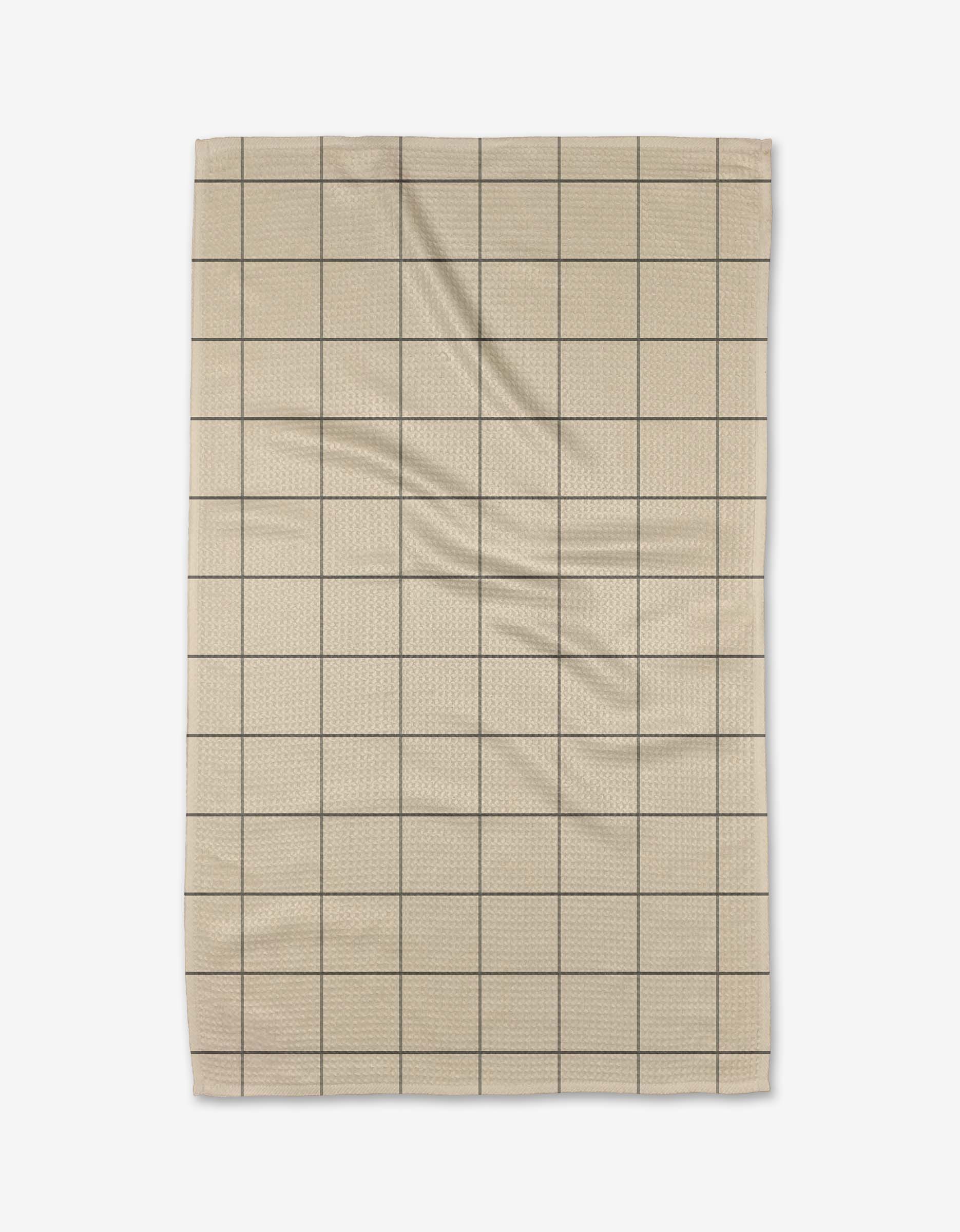 The Oat Grid tea towel by Kelsi Fullmer is made from beige Geoweave fabric with a grid of thin black lines forming squares. Slight wrinkles are visible, and it is photographed against a white background.