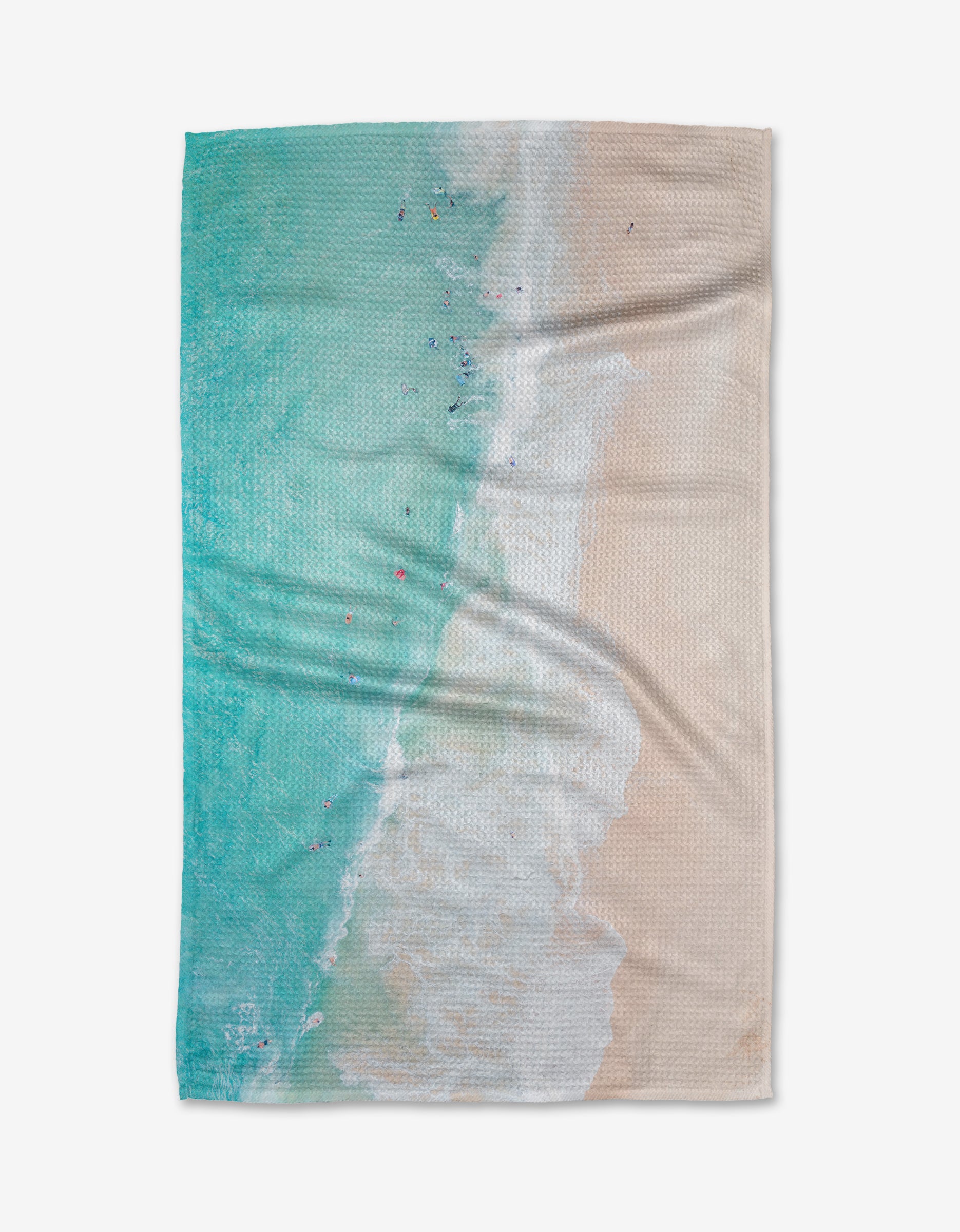 Out to Sea by Kait Hanson: This tea towel features an aerial beach view with turquoise water, white waves, and a sandy shore. Made from Geoweave™ fabric, it has small colorful dots for people or objects and a slightly wrinkled look.