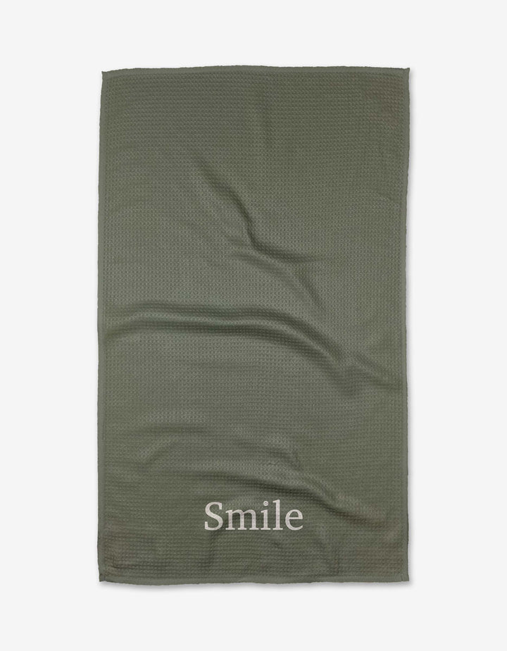 The Sage Smile tea towel by Kelsi Fullmer is green, textured, and made from recycled materials, featuring Smile printed in white near one edge and shown flat on a white background.