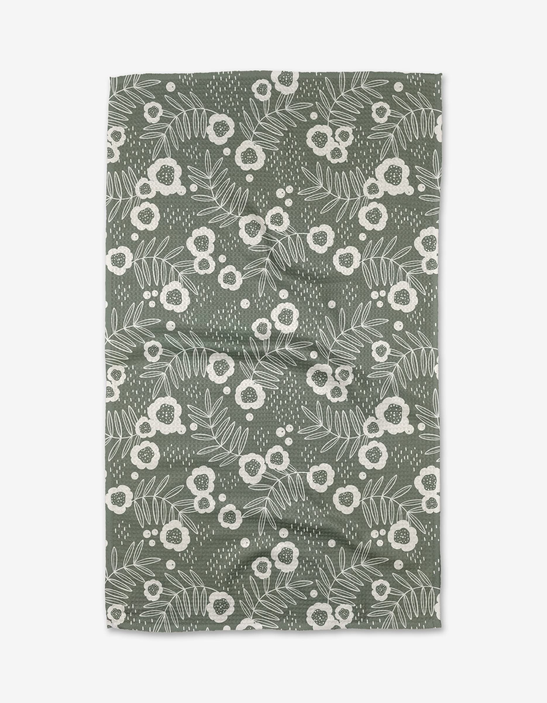 The Savannah Green tea towel by Charlie Rowan Designs features a rectangular Geoweave fabric with a white floral and leaf pattern of assorted flowers, leaves, and dots scattered over a green background.