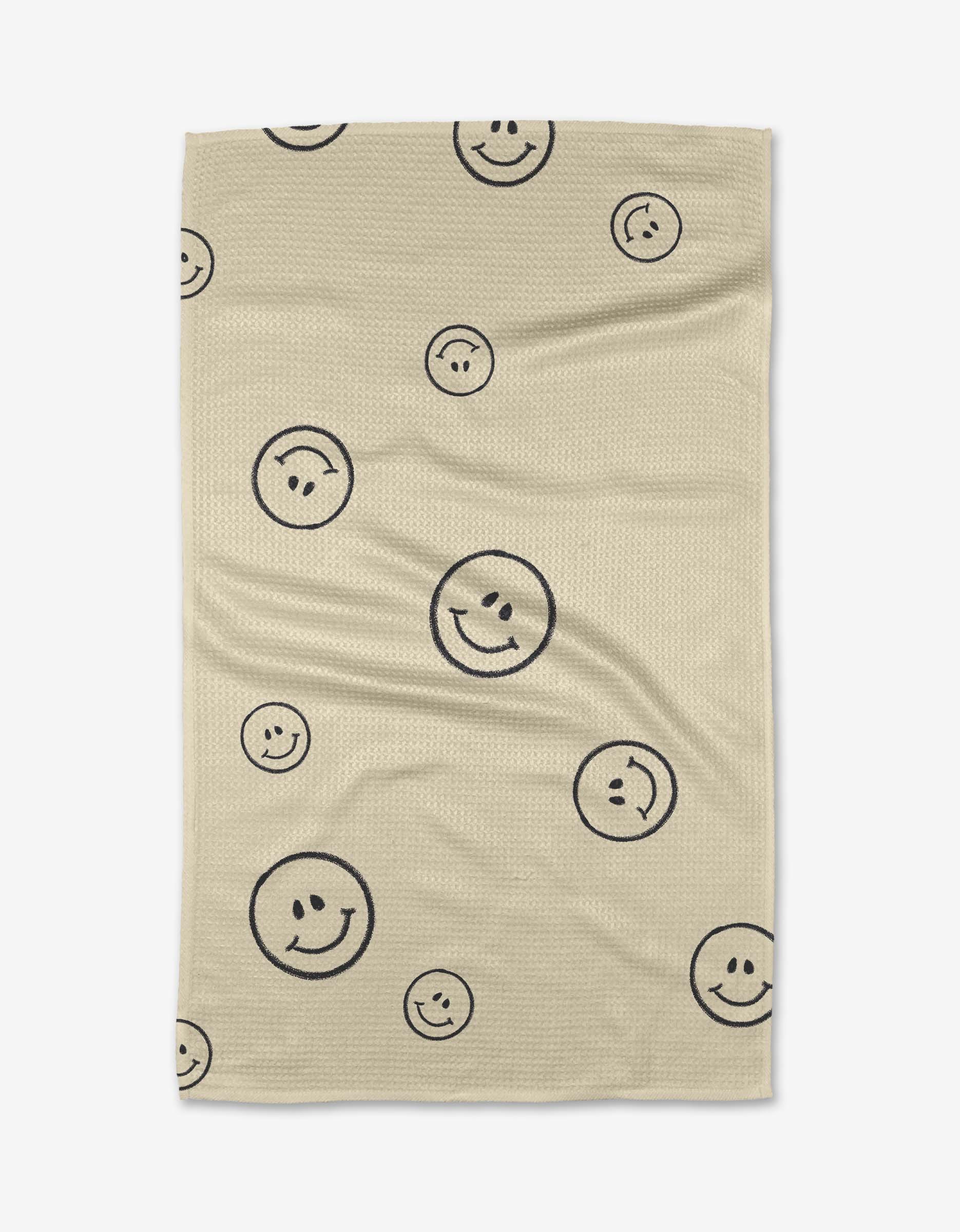 The Say Cheese blanket by Kelsi Fullmer is beige, made from recycled materials, and decorated with black outlined smiley faces in various sizes scattered across the surface.