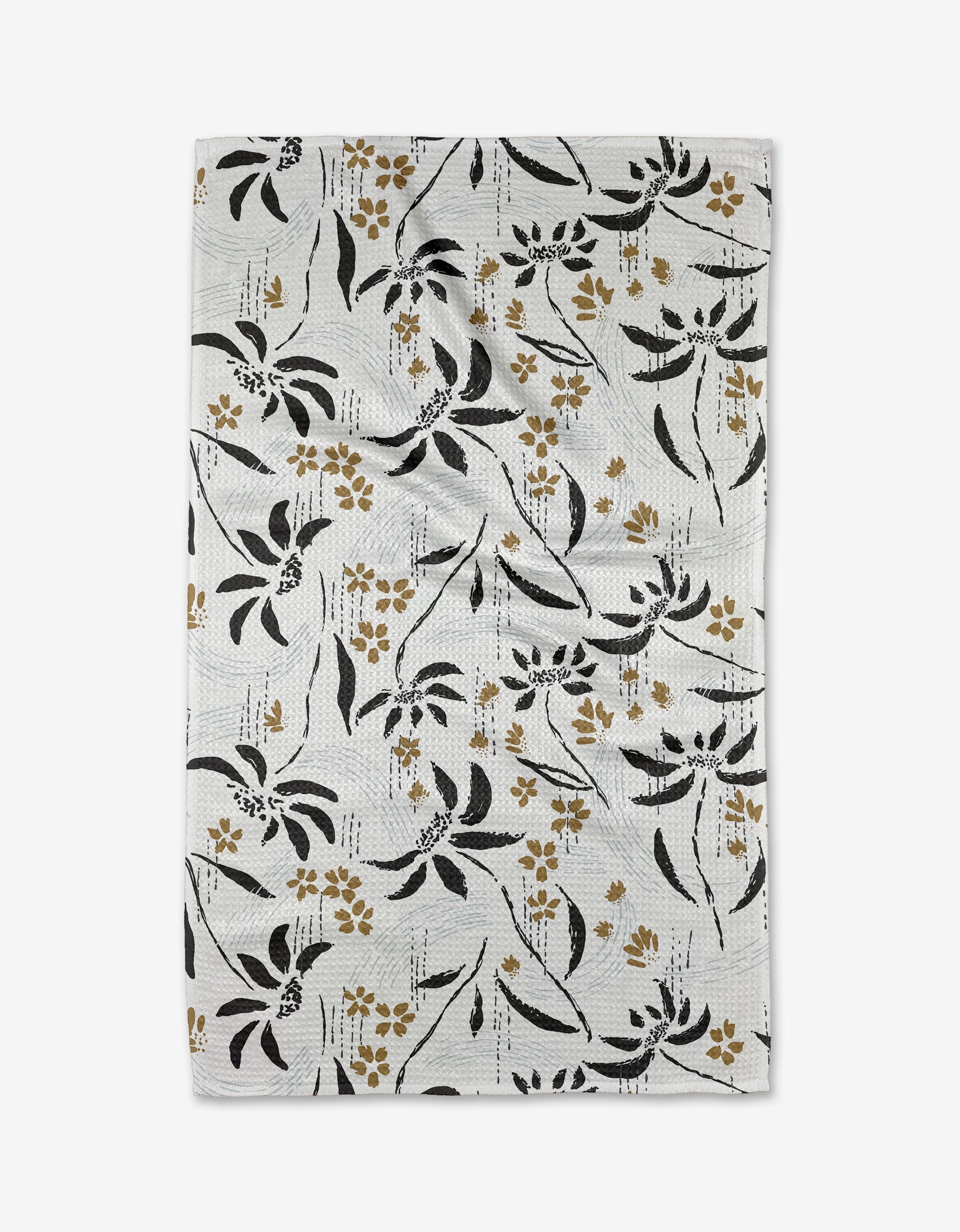 The Scenic tea towel by Toboggan Avenue features black and gold floral designs with scattered leaves and small flowers on white Geoweave™ fabric, set against a subtle striped backdrop.