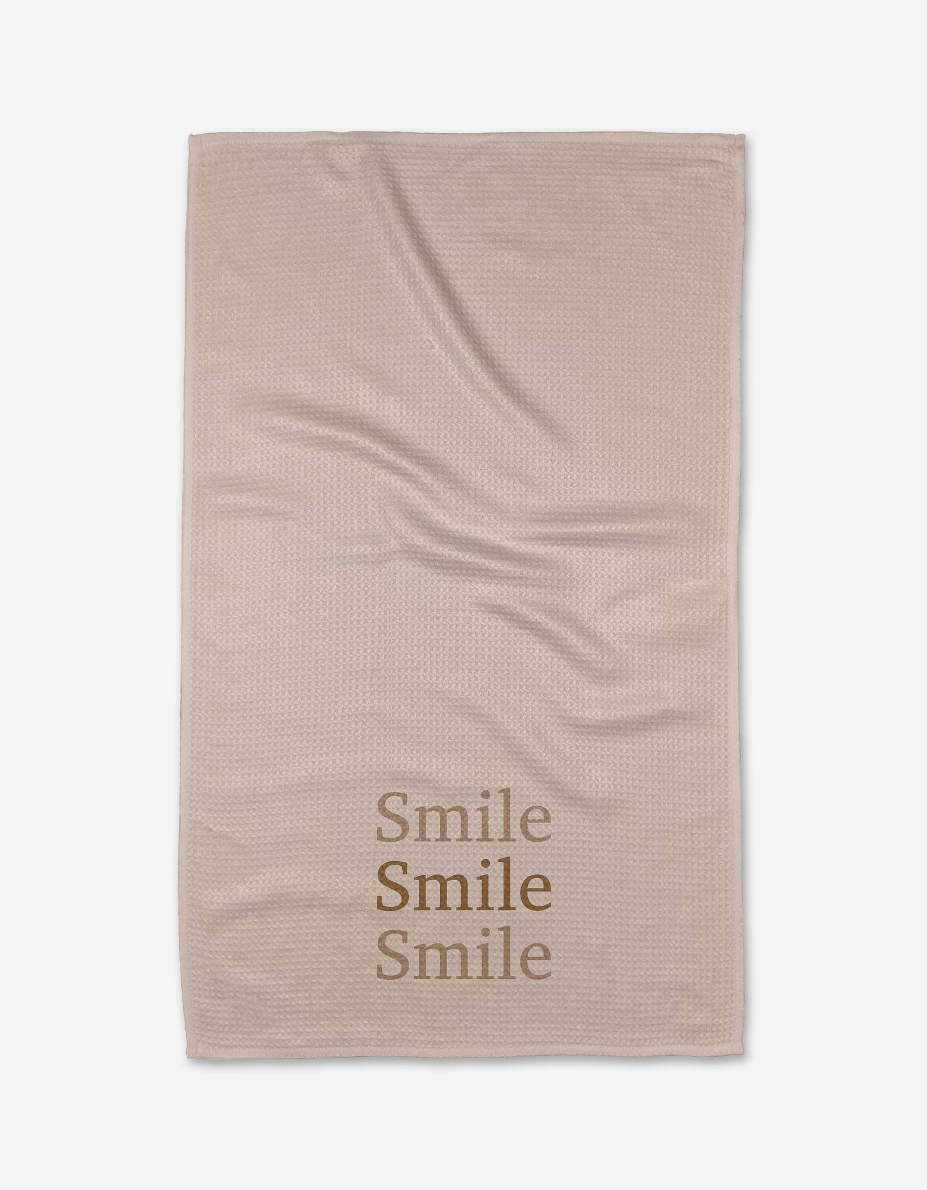 The Share A Smile tea towel by Kelsi Fullmer is beige with a slightly wrinkled look. Smile is printed three times in brown near one corner. Made from recycled materials, its an eco-friendly option for your kitchen.
