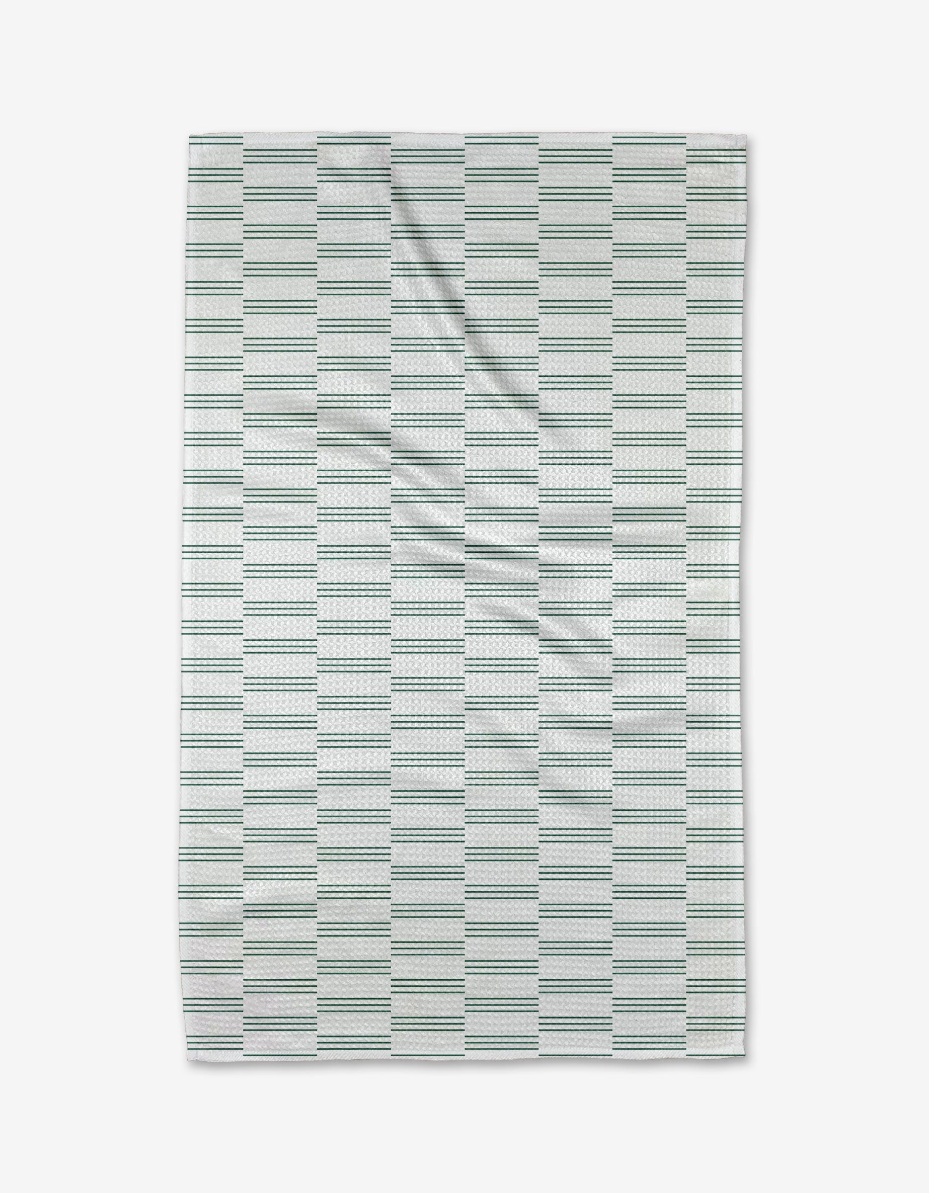 The Buy Guide’s Small Stripe - Evergreen tea towel features a white background with thin green and blue stripes in rectangular blocks. Crafted from Geoweave fabric, it’s pictured laid flat with subtle wrinkles.
