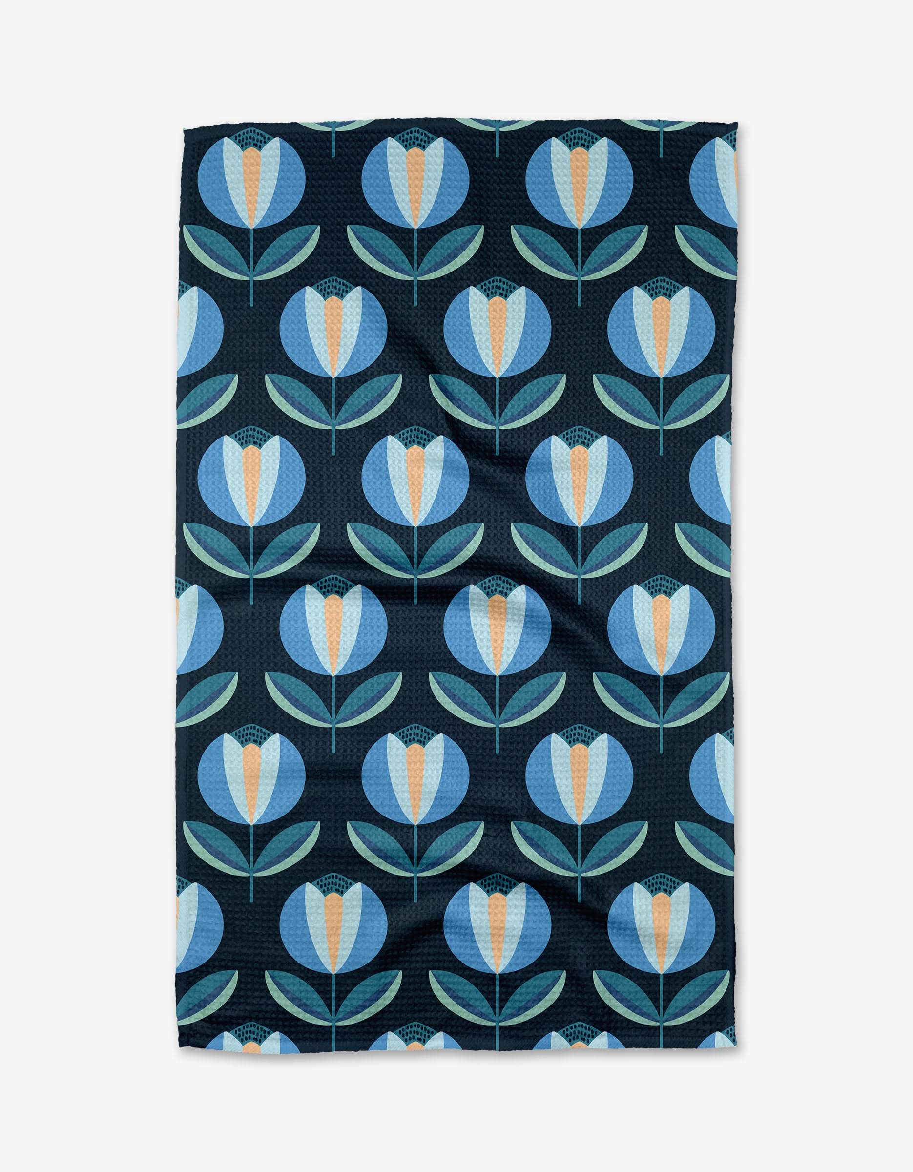 The Blissful Flamingo Spring Florals Tea Towel is made from recycled materials and features a repeating pattern of stylized blue and light blue flowers with orange centers and green leaves on a dark background.