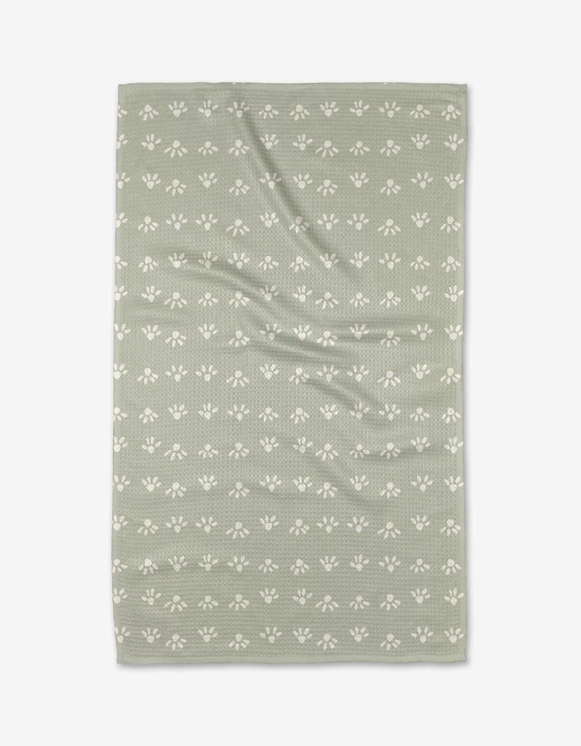 The Anee Shah Sun Bursts tea towel is green, rectangular, made from recycled materials, and features a textured surface with rows of small white paw prints across the fabric.