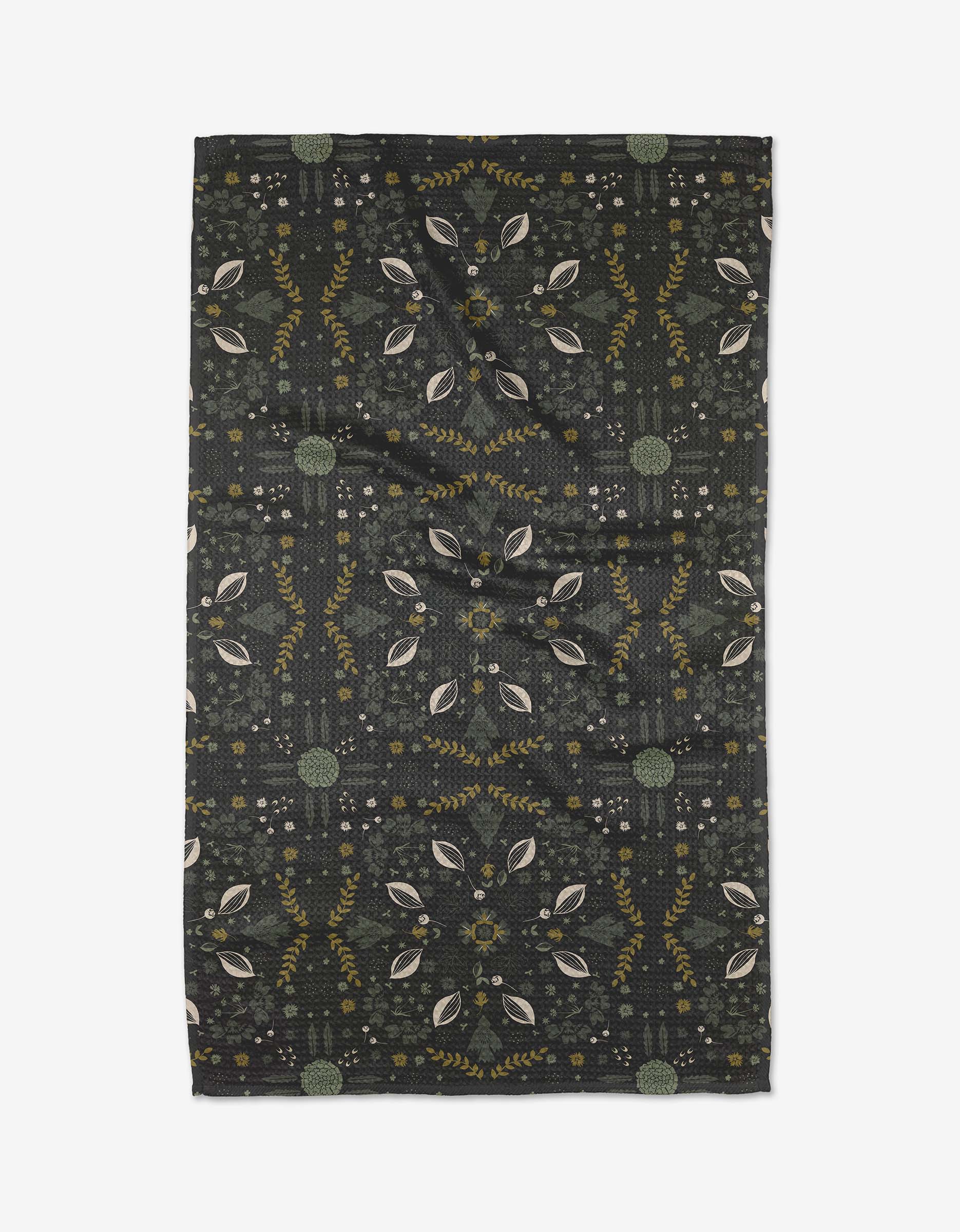 The Ash Cascade Trailhead tea towel is rectangular and dark, with a symmetrical leaf and botanical pattern in muted green, yellow, and beige. Made from eco-friendly fabric, it has gentle wrinkles and is shown flat on a white background.