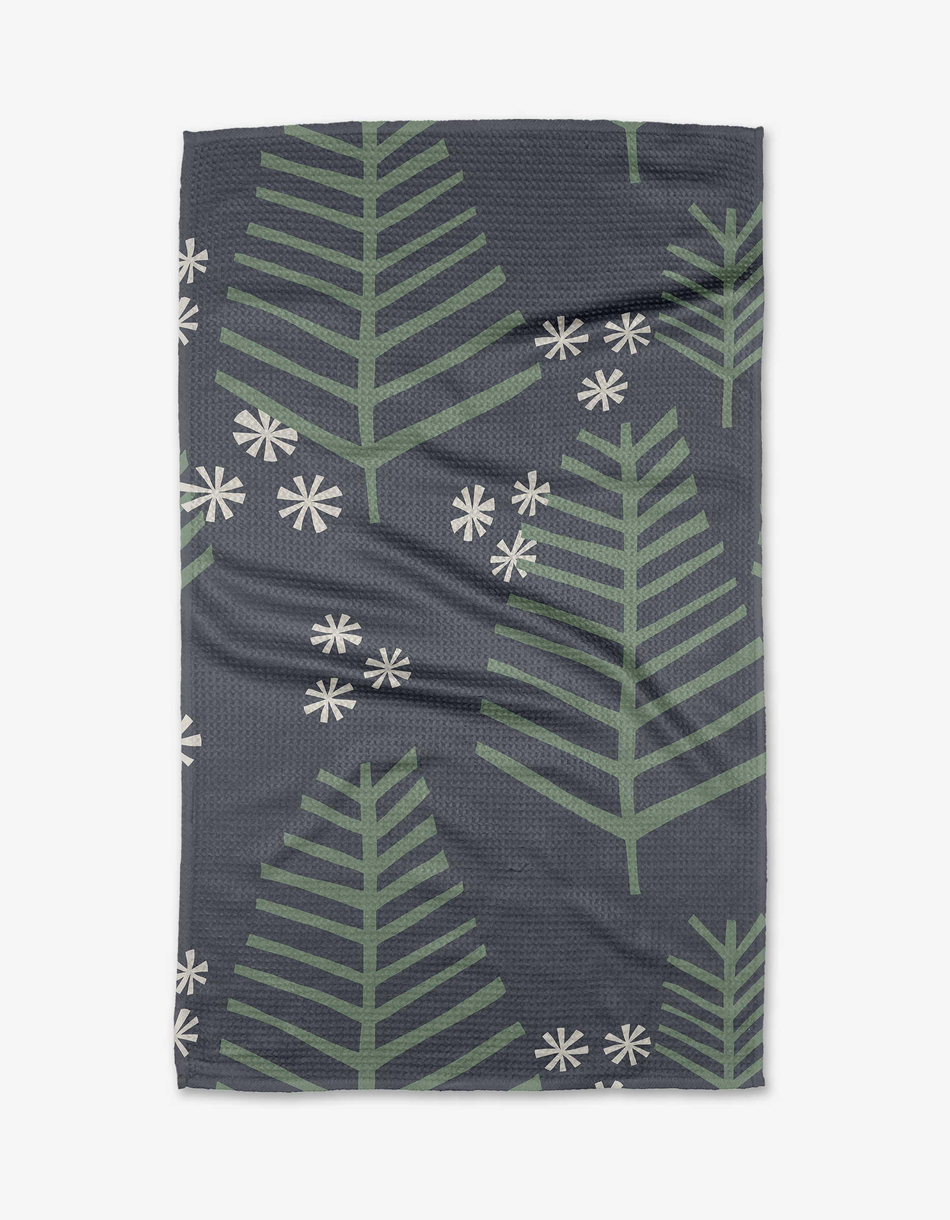 The Lizzie Clark Triple Trees Tea Towel features large green pine branches and white snowflakes on dark gray Geoweave fabric made with post-consumer recycled materials.