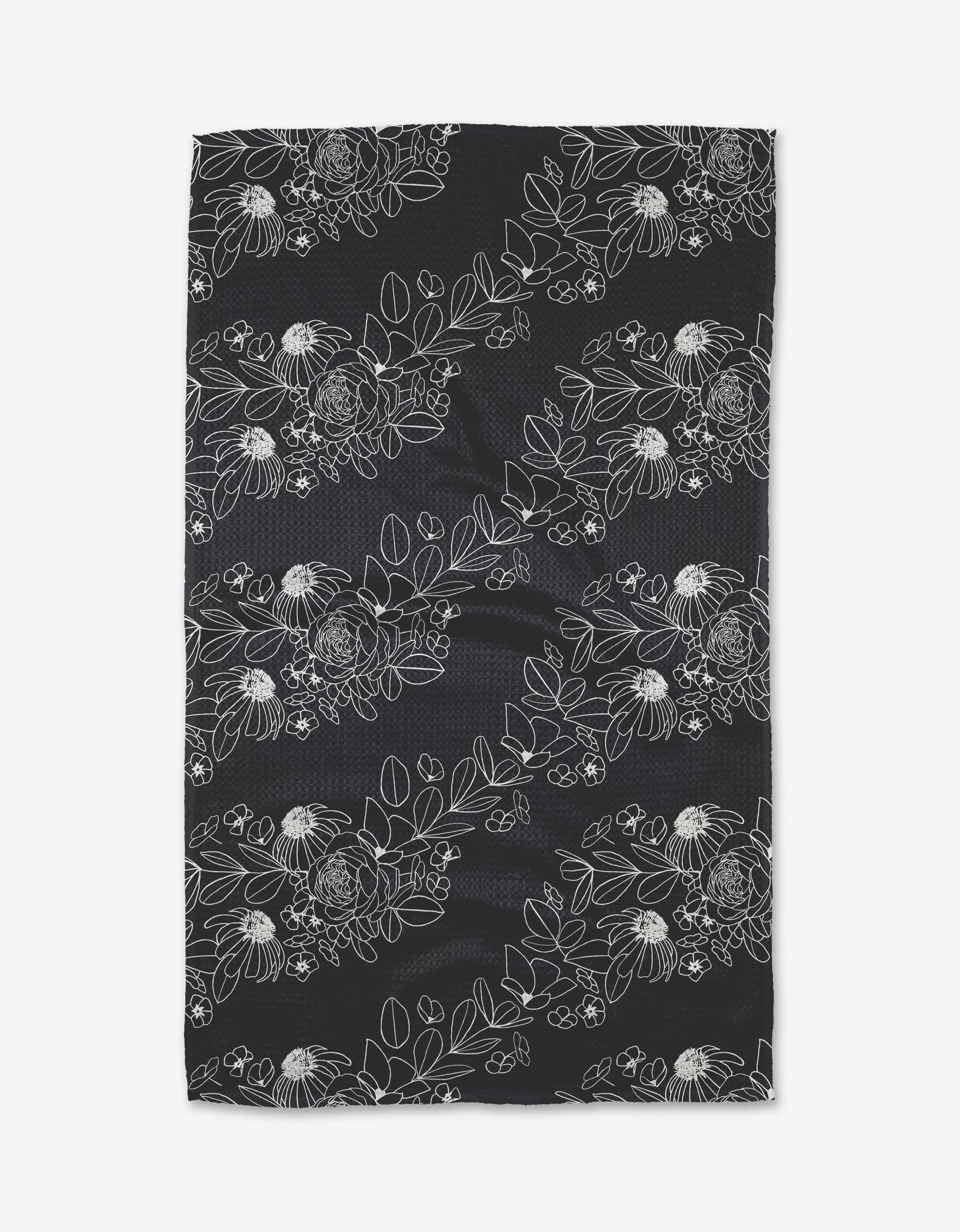 The Wild and Wonderful Tea Towel by Rosa Kichline is black, rectangular, made from recycled materials, and features white minimalist floral and leafy line drawings arranged diagonally.