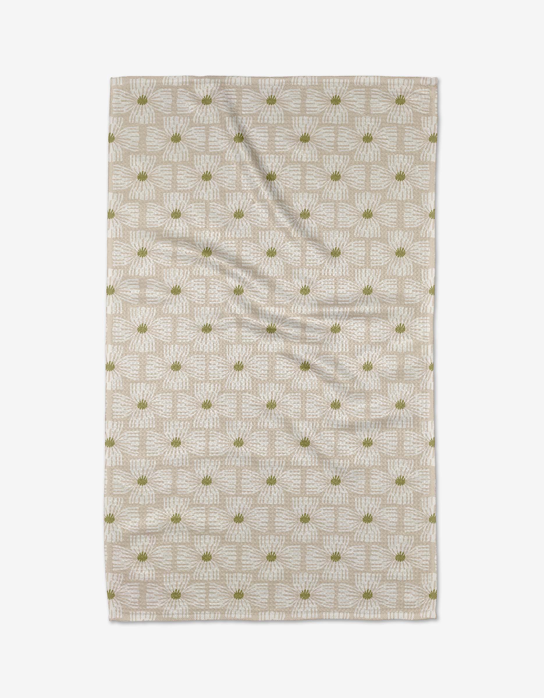 The Ash Cascade Wildflower tea towel is a beige rectangle made from Geoweave fabric, decorated with a white geometric pattern and small green floral accents, shown flat on a white background.