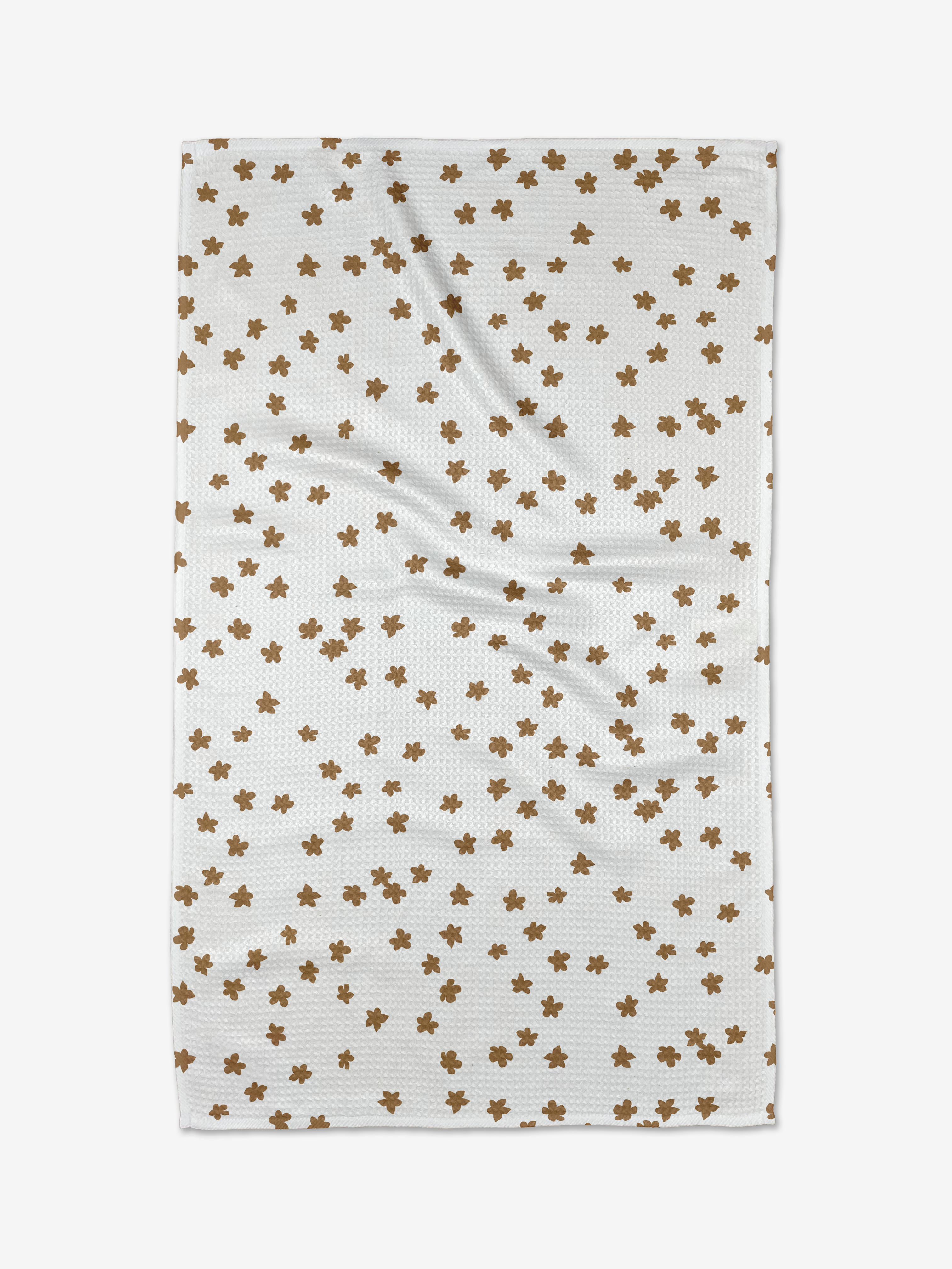The Julianne Haness Haness Golden is a white kitchen towel with a textured pattern and scattered small brown flowers. Made from recycled materials, the towel shows slight wrinkles when laid flat.