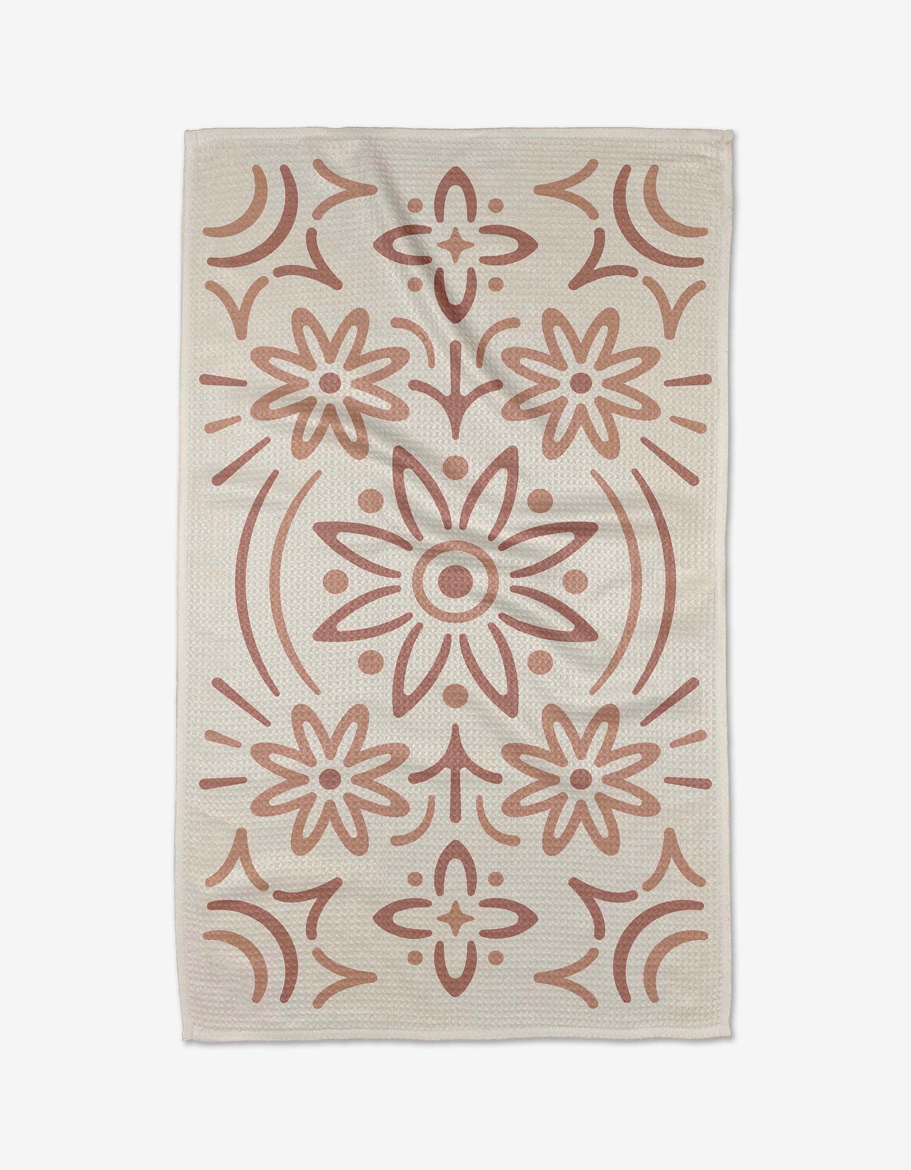 The Blossom rug by Adam Nienow is a beige, rectangular piece with a centered and symmetrical pattern of large, stylized flowers and geometric shapes in muted terracotta, evoking the look of recycled kitchen towel designs.
