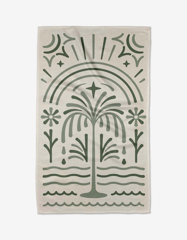 The Solana tea towel by Adam Nienow features a stylized green palm tree, flowers, waves, and an arch on beige. Made from quick-drying recycled materials for eco-friendly style.